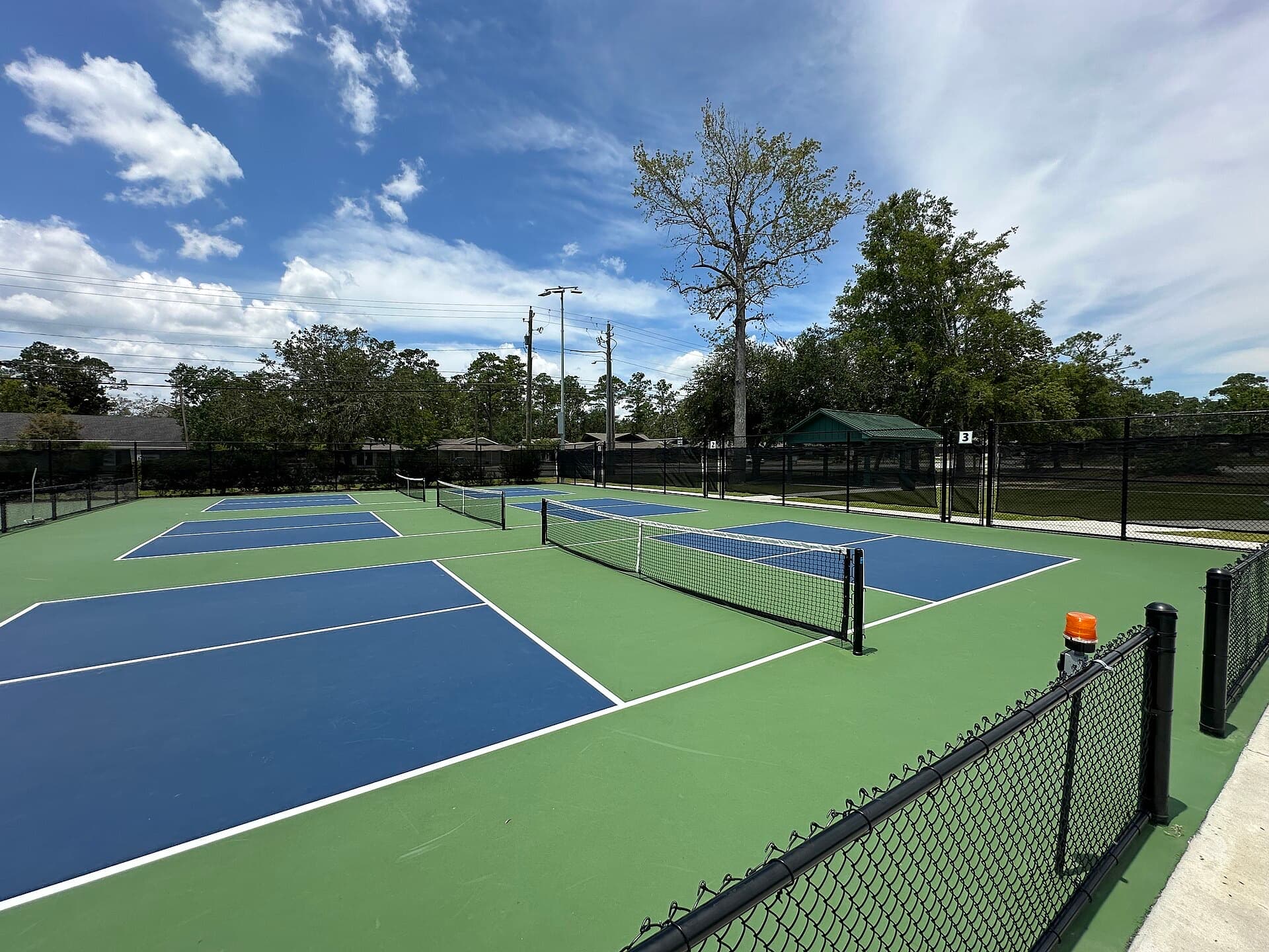 Outdoor pickleball courts with blue playing surfaces and nets under a sunny sky